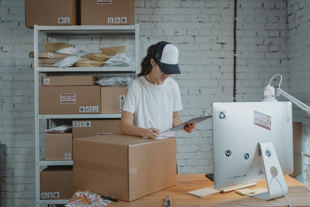Image of Woman writing down on a Carton Box while looking at a Clipboard